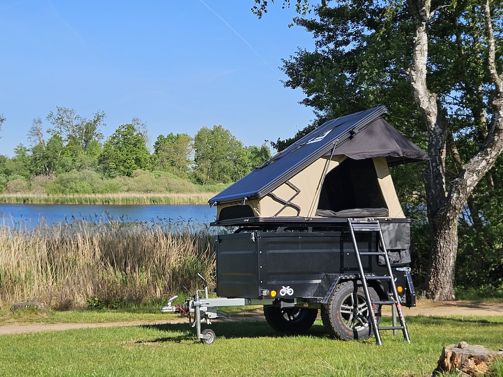 Groenberg Tjelvar hard-shell rooftop tent open on a trailer by a lake