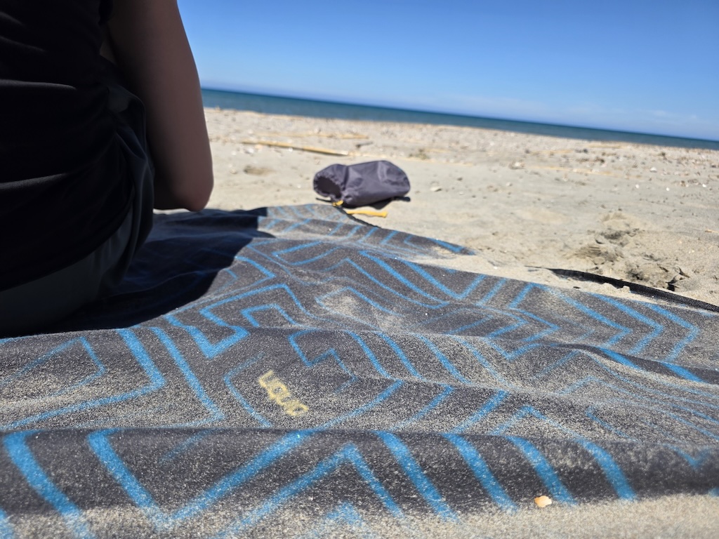 Kind sitzt von hinten auf der SCOTTY Picknickdecke am Strand in Sardinien – Nahaufnahme