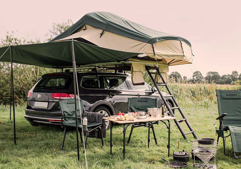 Halvor 160 aufgeklappt auf einem Auto, daneben Tisch und Stühle unter einem Tarp