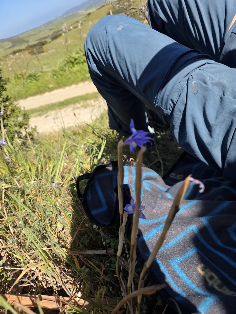 Kind sitzt auf der uquip SCOTTY Picknickdecke auf einer grünen Wiese in Sardinien